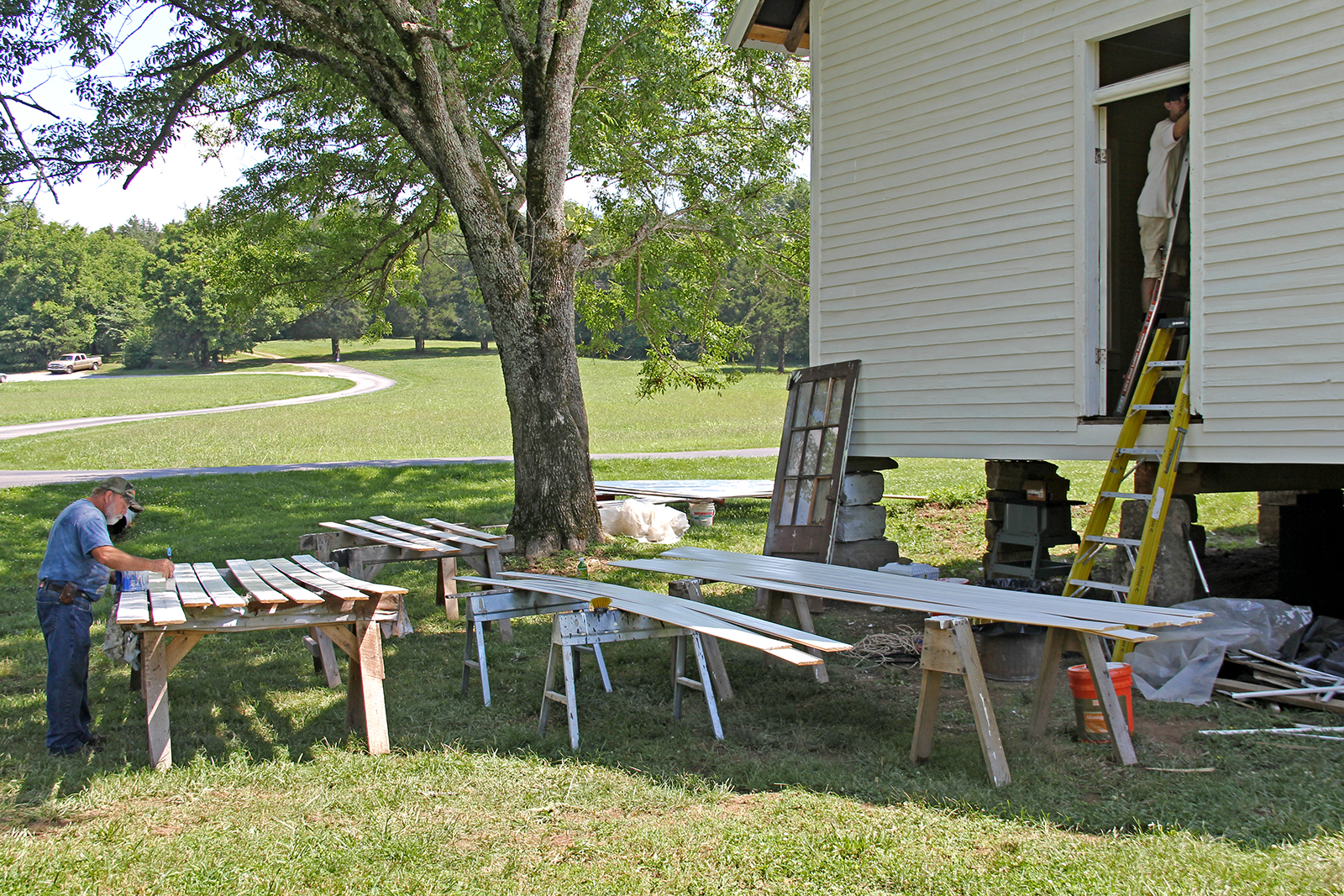 Man painting boards outside front of one-room schoolhouse on Foxfire Farm in Lynnville, TN