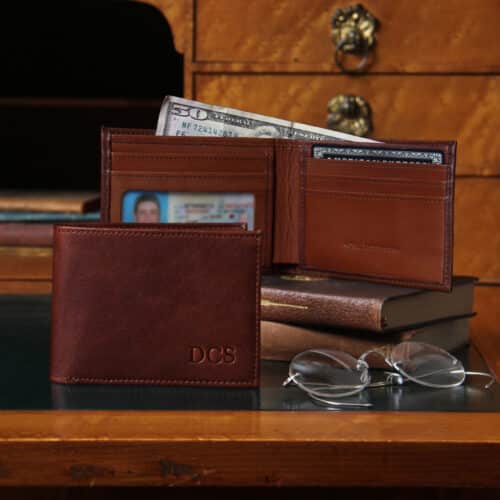 No. 4 Billfold Wallet in Vintage Brown American Steerhide - 2 wallets on an antique desk next to vintage spectacles - Front wallet to the left, closed, showing 3 embossed initials - back wallet, center right, open and showing driver's license, a credit card, and cash