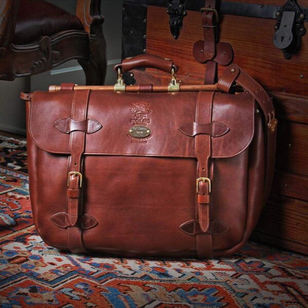 No. 83 Book Bag Leather Briefcase in Vintage Brown American Steerhide sitting against a vintage steamer trunk on an antique oriental carpet