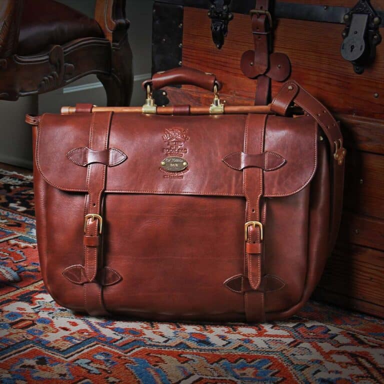 No. 83 Book Bag Leather Briefcase in Vintage Brown American Steerhide sitting against a vintage steamer trunk on an antique oriental carpet