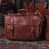 No. 83 Book Bag Leather Briefcase in Vintage Brown American Steerhide sitting against a vintage steamer trunk on an antique oriental carpet