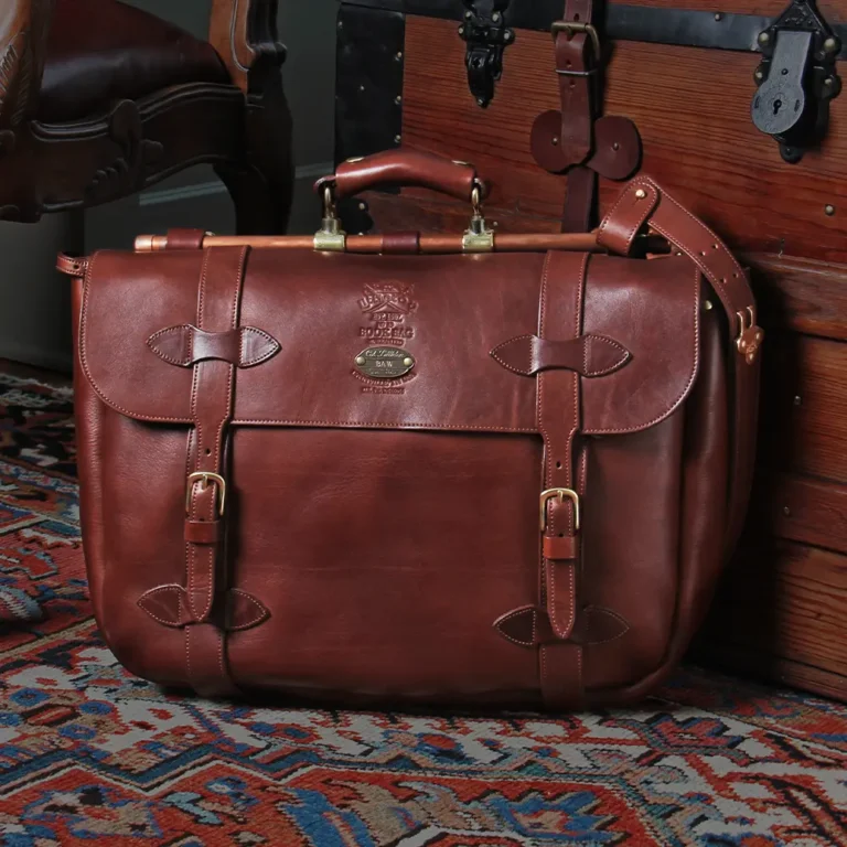 No. 83 Book Bag Leather Briefcase in Vintage Brown American Steerhide sitting against a vintage steamer trunk on an antique oriental carpet