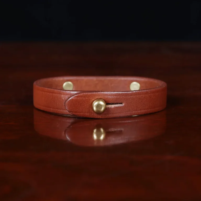 camp bracelet in vintage brown leather on a wooden table and a dark background - brass - back view