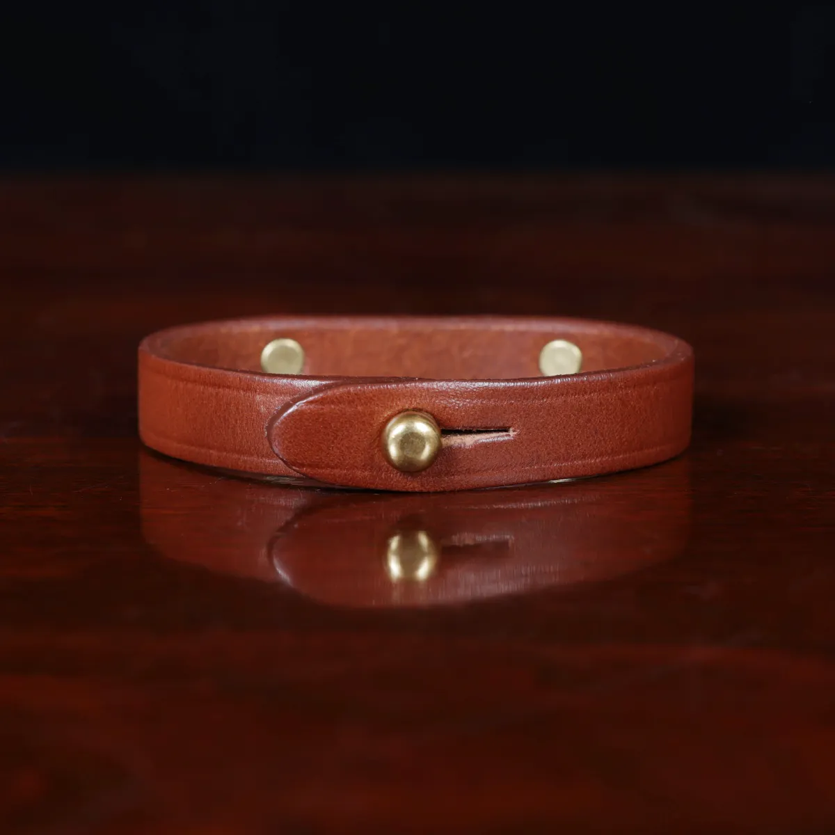 camp bracelet in vintage brown leather on a wooden table and a dark background - brass - back view