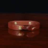 camp bracelet in vintage brown leather on a wooden table and a dark background - brass - back open view