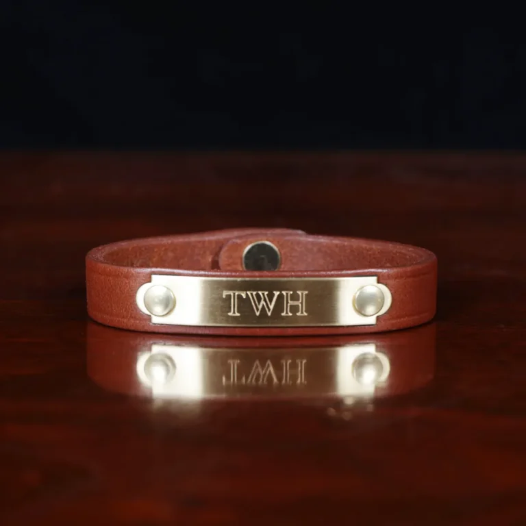 camp bracelet in vintage brown leather on a wooden table and a dark background - brass plates