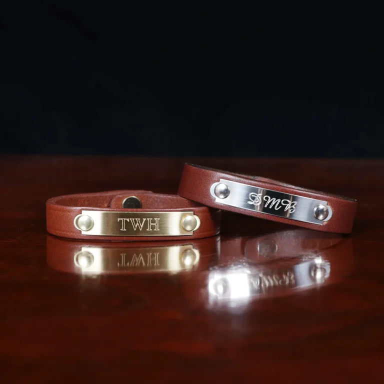 camp bracelets in vintage brown leather on a wooden table and a dark background - nickel and brass plates