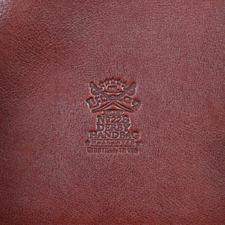 No. 22B Derby Handbag in Vintage Brown on a wood table with a dark background - back view of logo