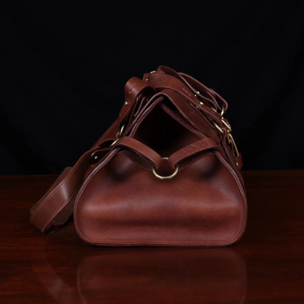 leather travel bag - side view- on a wooden table with a dark background