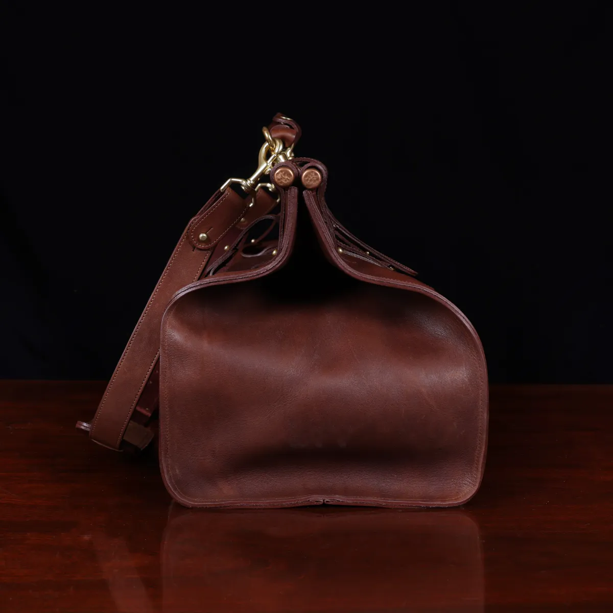 Vintage-style dark brown No. 3 Grip Bag on wooden table with a dark background - side view