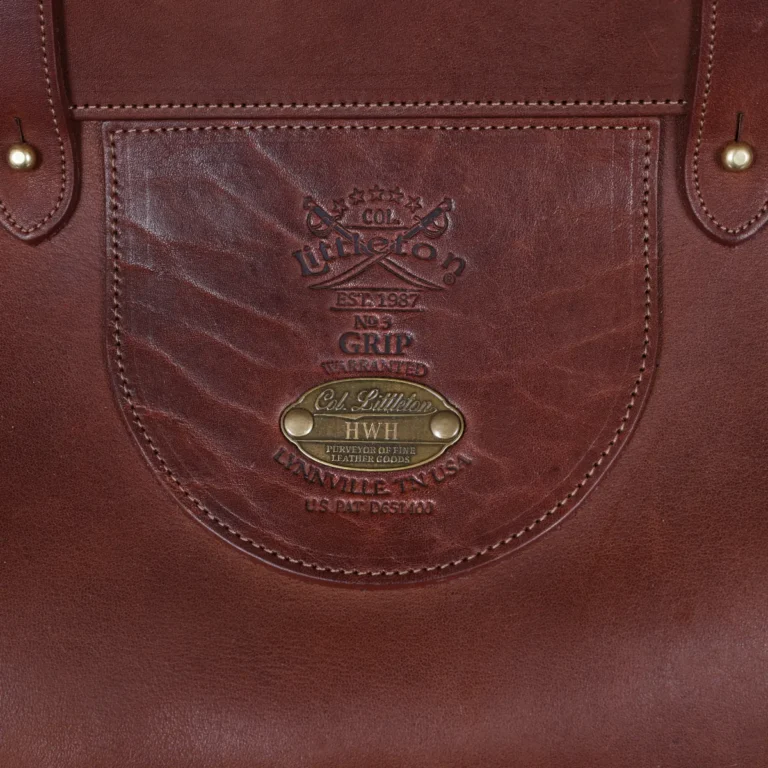 Vintage-style dark brown No. 3 Grip Bag on wooden table with a dark background - view of logo