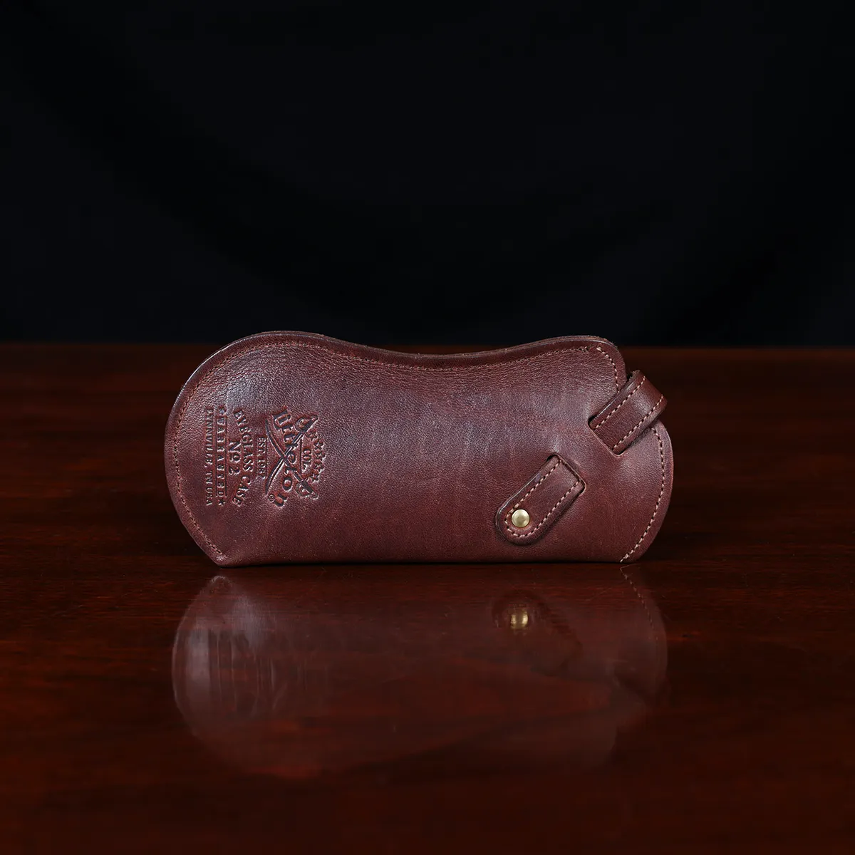 Brown leather No. 2 Eyeglass Case on top of a wooden table with a dark background - back view