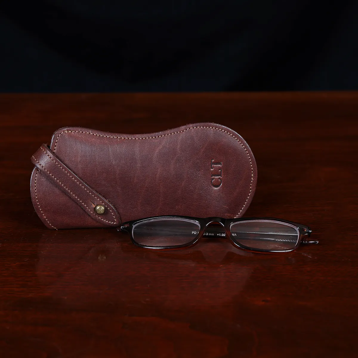 Brown leather No. 2 Eyeglass Case on top of a wooden table with a dark background with glasses