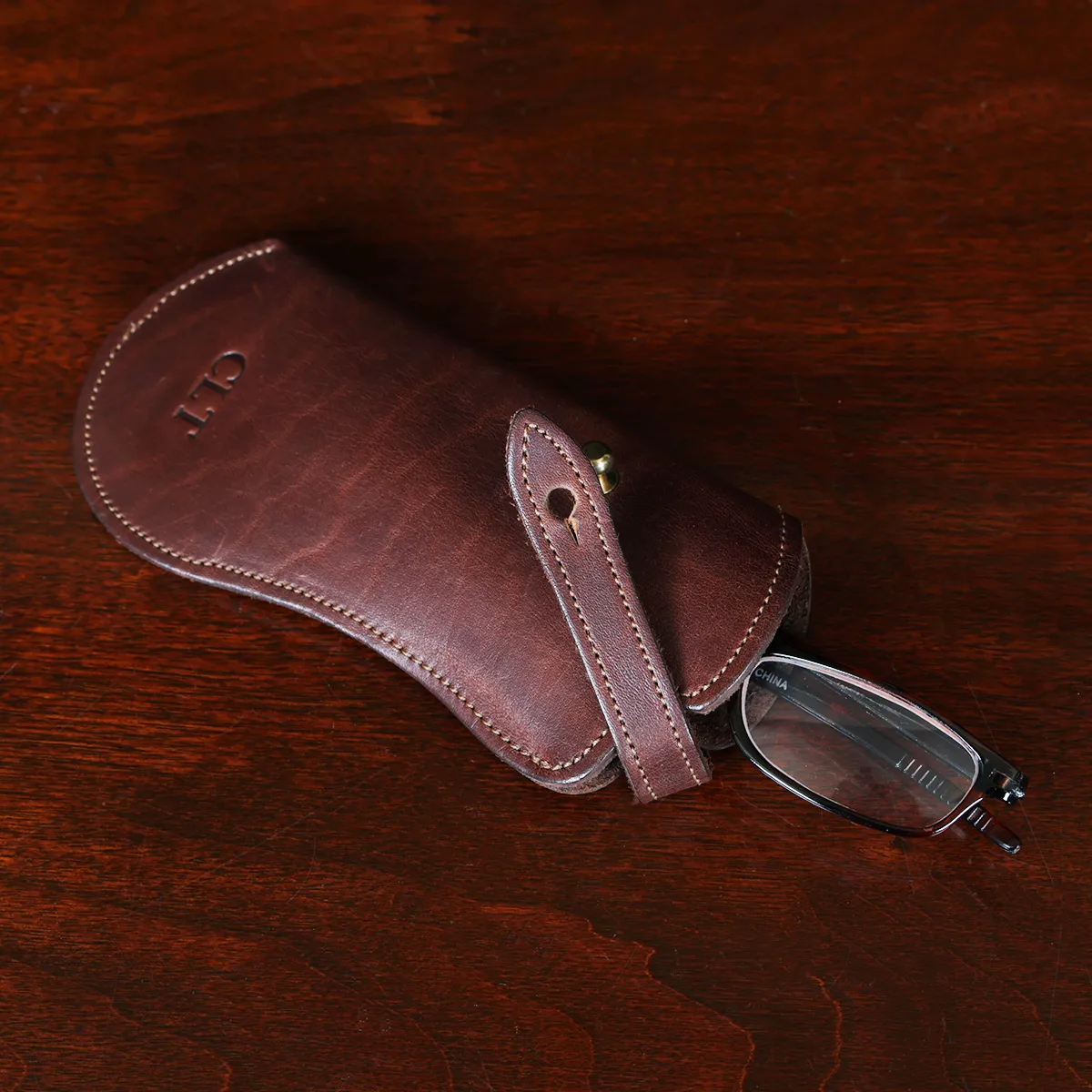 Brown leather No. 2 Eyeglass Case on top of a wooden table with a dark background open with glasses
