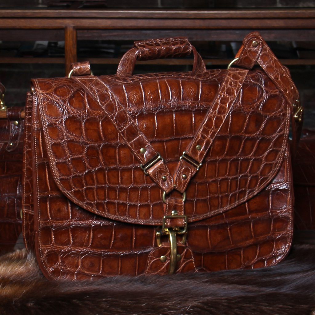 No. 41 Commander Briefcase in Vintage Brown American Alligator sitting on a dark brown fur-draped steamer trunk