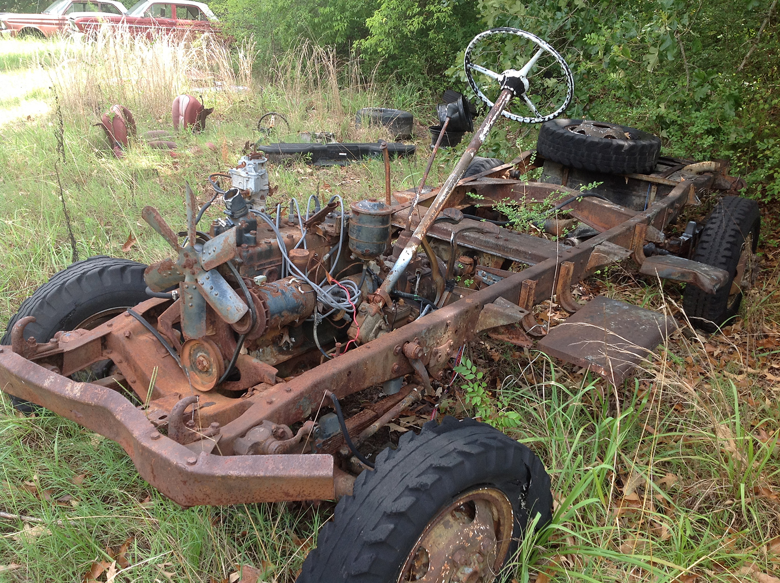 Rusted out chassis of a 1941 Army Command Car overgrown with weeds.