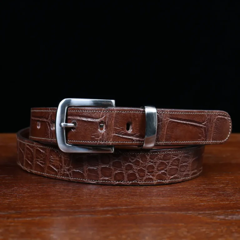 An American Alligator Belt with Nickel hardware showing the front coiled view on a wooden table with black background - id 001