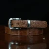 An American Alligator Belt with Nickel hardware showing the front coiled view on a wooden table with black background - id 001