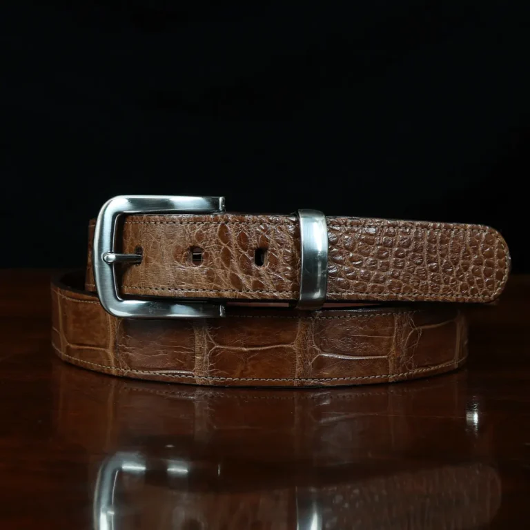 An American Alligator Belt with Nickel hardware showing the front coiled view on a wooden table with black background - id 001