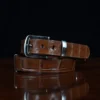 An American Alligator Belt with Nickel hardware showing the coiled front view on a wooden table with black background - id 001
