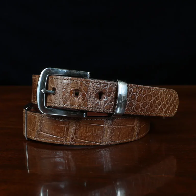 An American Alligator Belt with Nickel hardware showing the coiled front view on a wooden table with black background - id 001