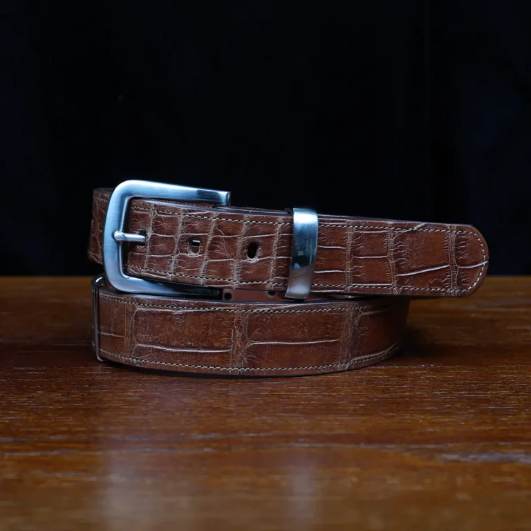 An American Alligator Belt with Nickel hardware showing the coiled front view on a wooden table with black background - id 001