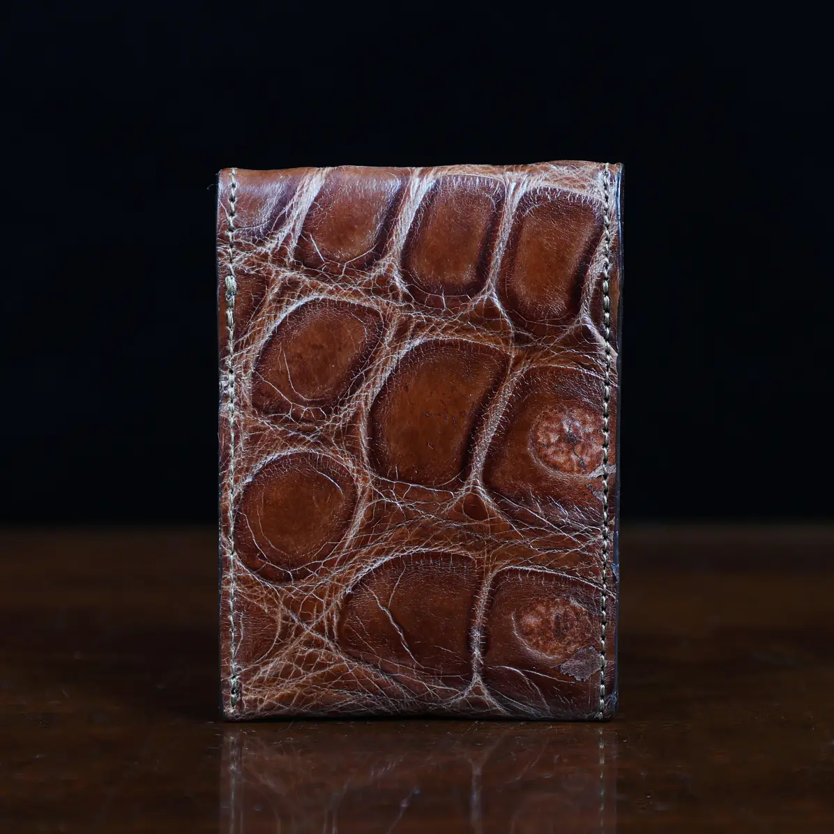 View larger image of Front pocket wallet with flap in brown American Alligator - back view - 001 - on wood table with a dark background