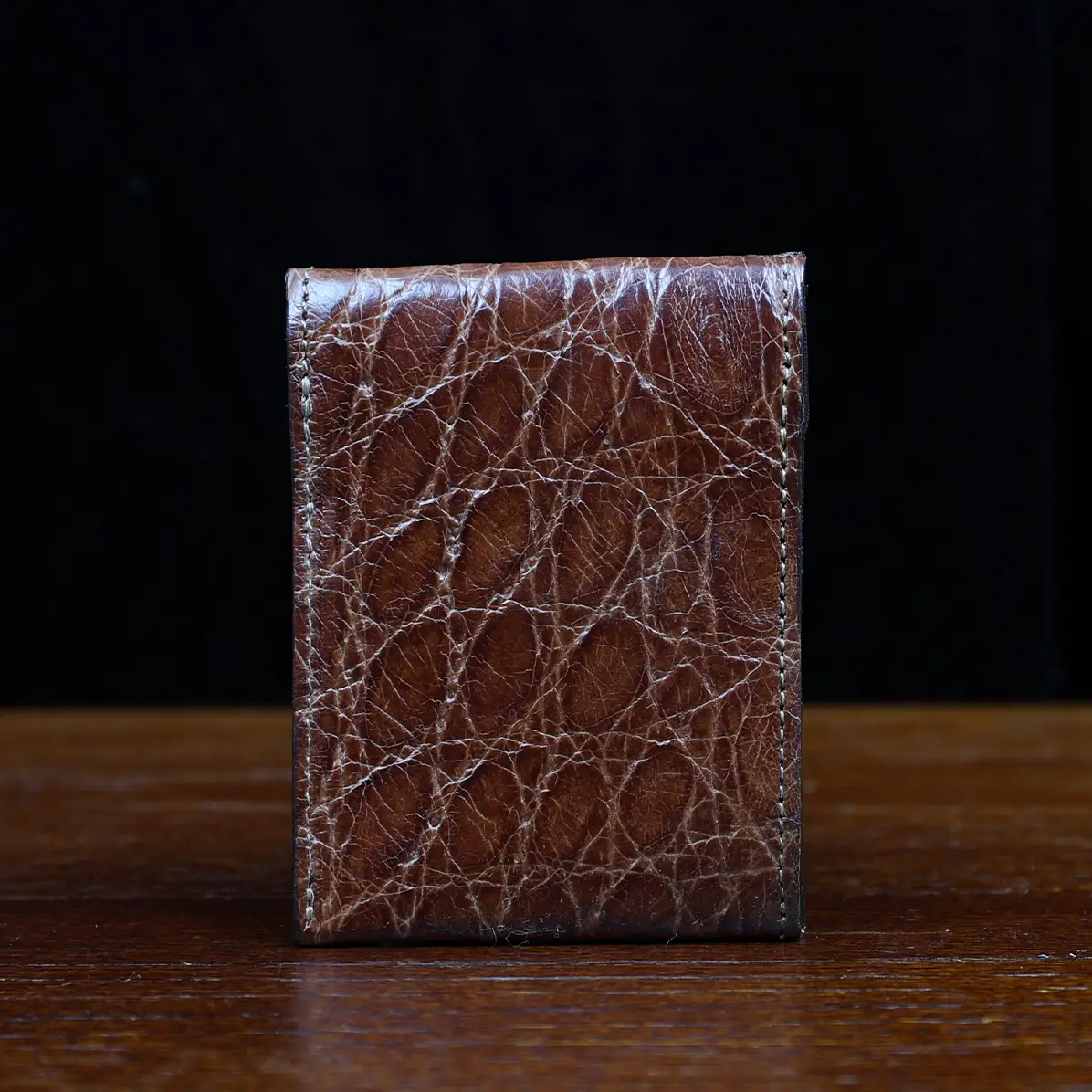 View larger image of Front pocket wallet with flap in brown American Alligator - back view - 001 - on wood table with a dark background