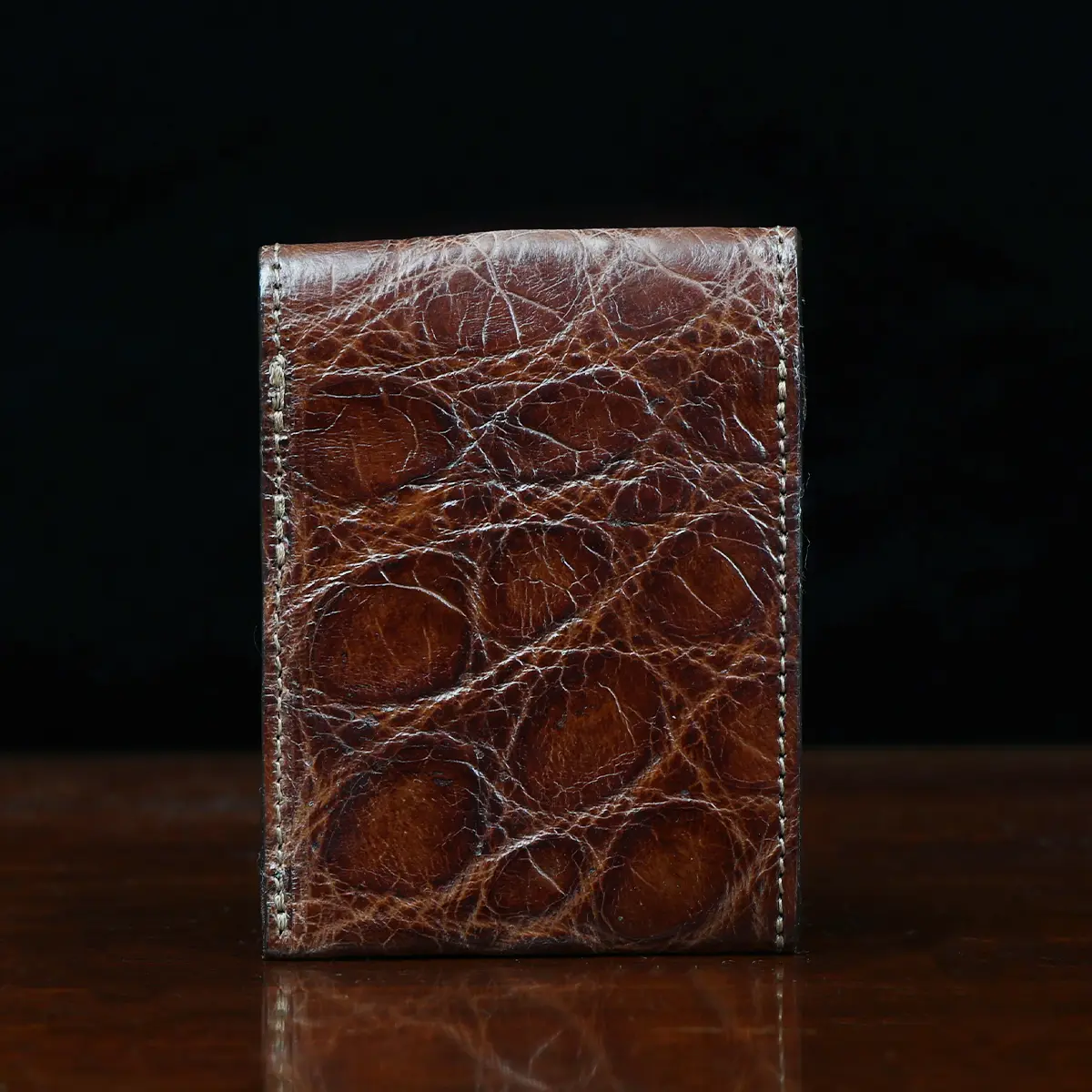 View larger image of Front pocket wallet with flap in brown American Alligator - back view - 001 - on wood table with a dark background