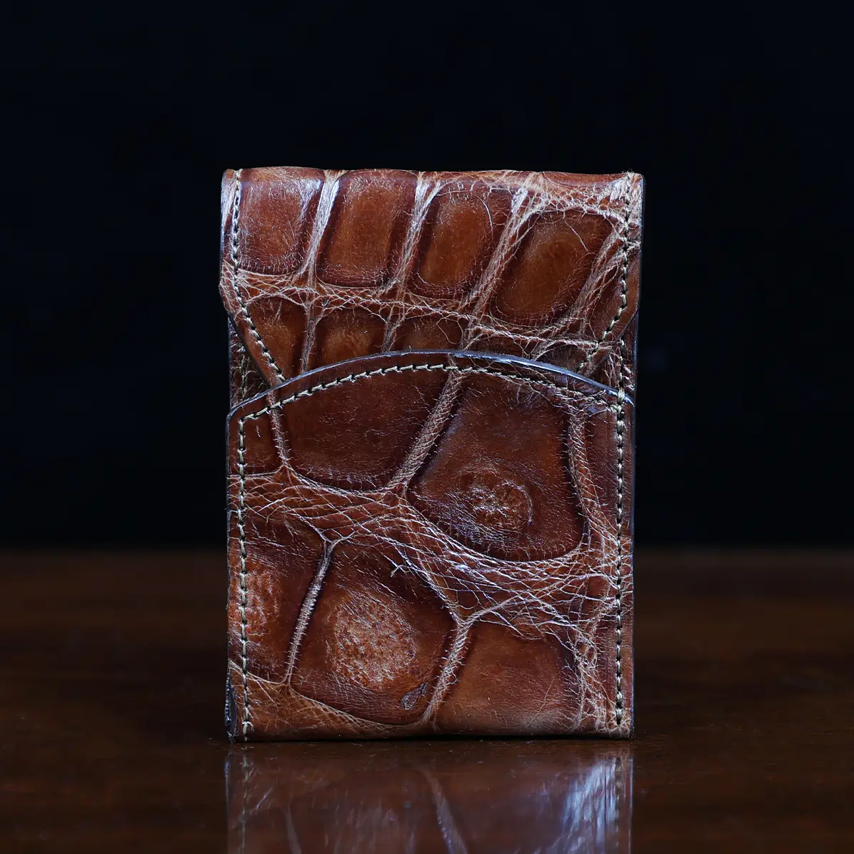 View larger image of Front pocket wallet with flap in brown American Alligator - front view - 001 - on wood table with a dark background