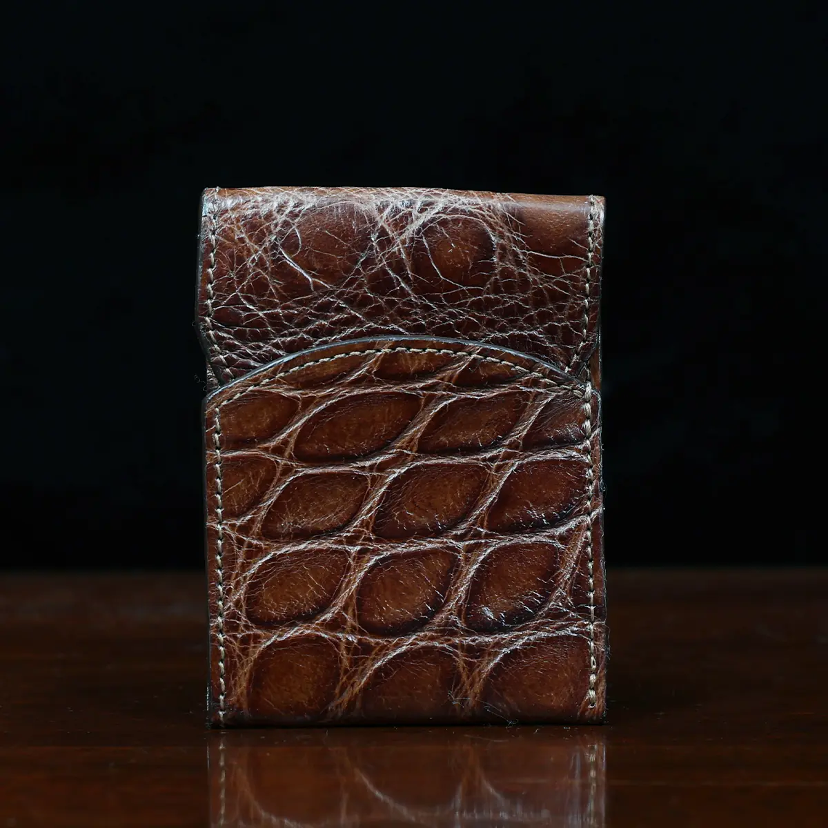 View larger image of Front pocket wallet with flap in brown American Alligator - front view - 001 - on wood table with a dark background