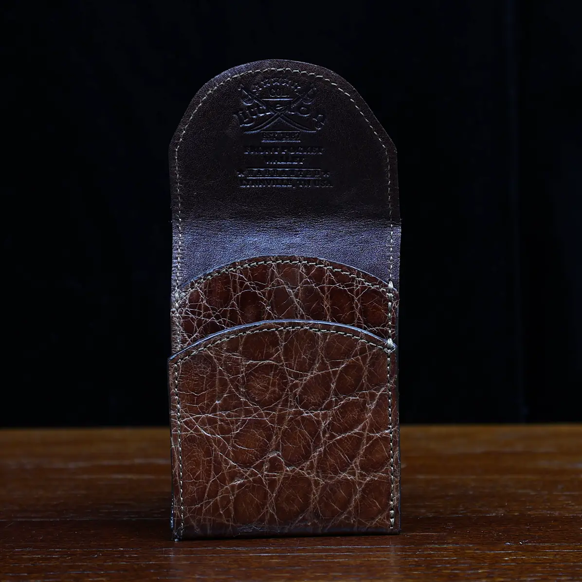 View larger image of Front pocket wallet with flap in brown American Alligator - front view - 001 - on wood table with a dark background