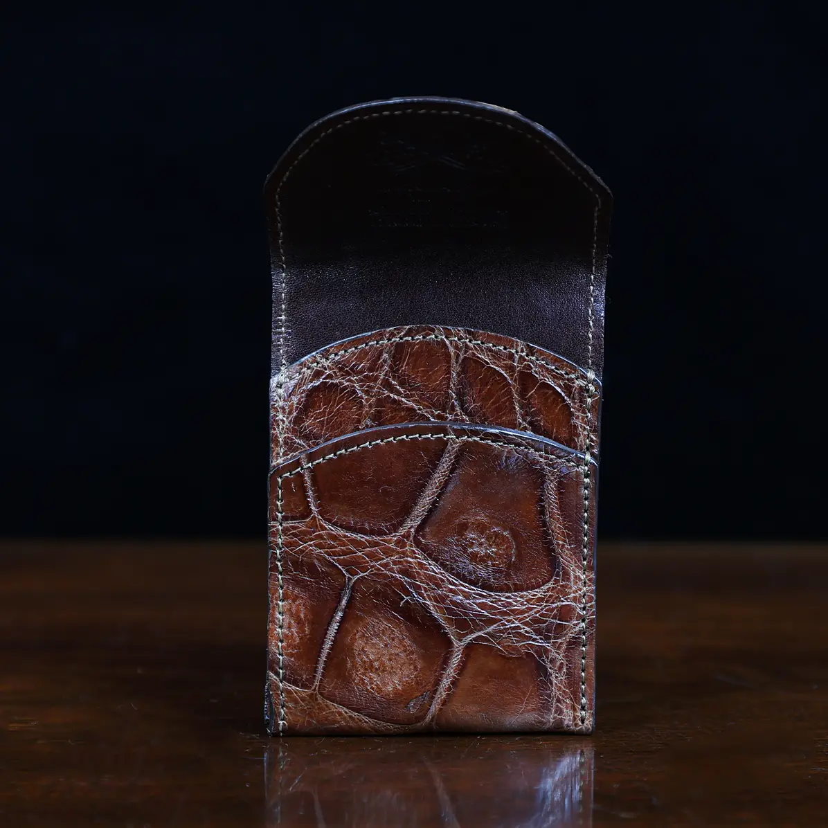 View larger image of Front pocket wallet with flap in brown American Alligator - front view - 001 - on wood table with a dark background