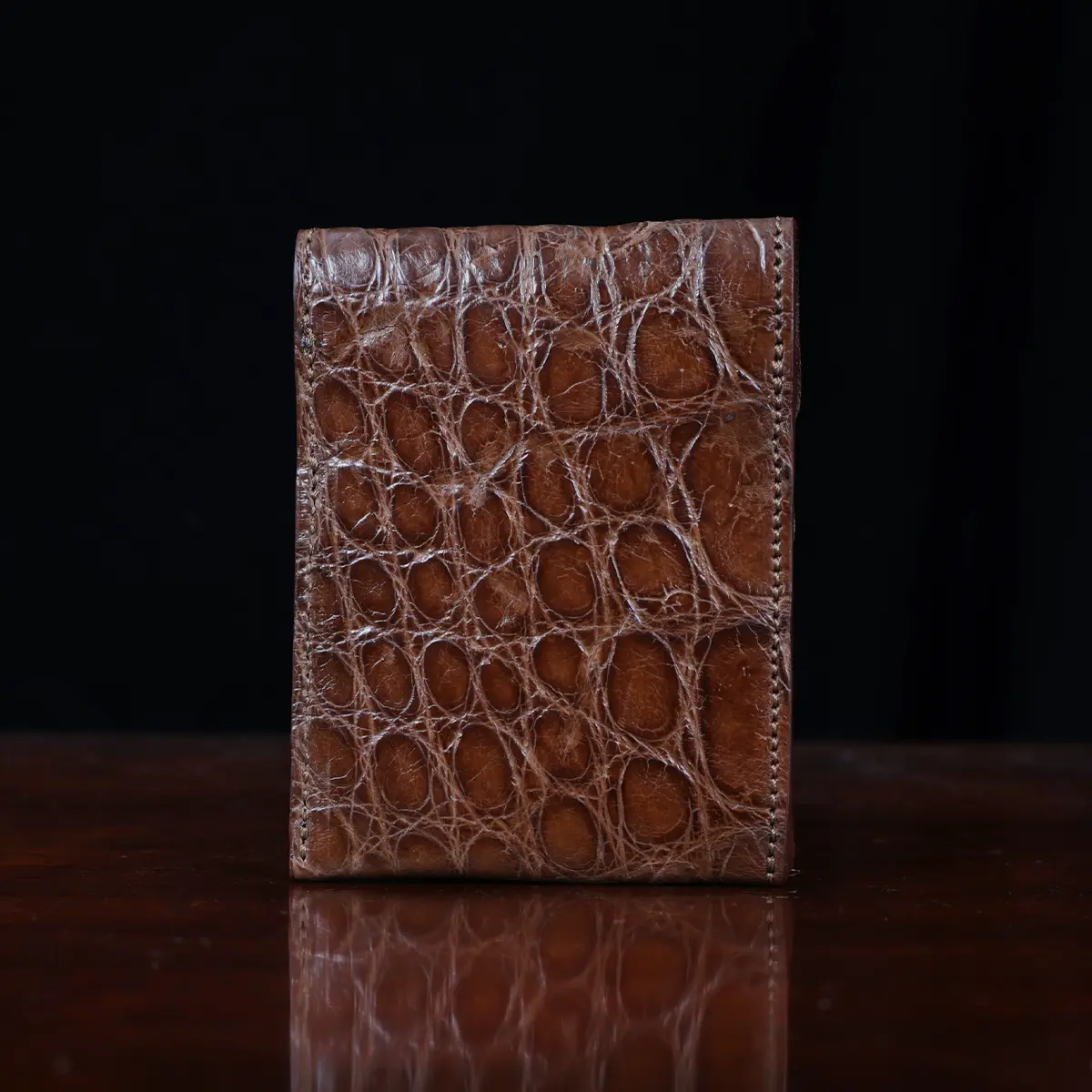 Front pocket wallet with flap in brown American Alligator - back view - 002 - on wood table with a dark background