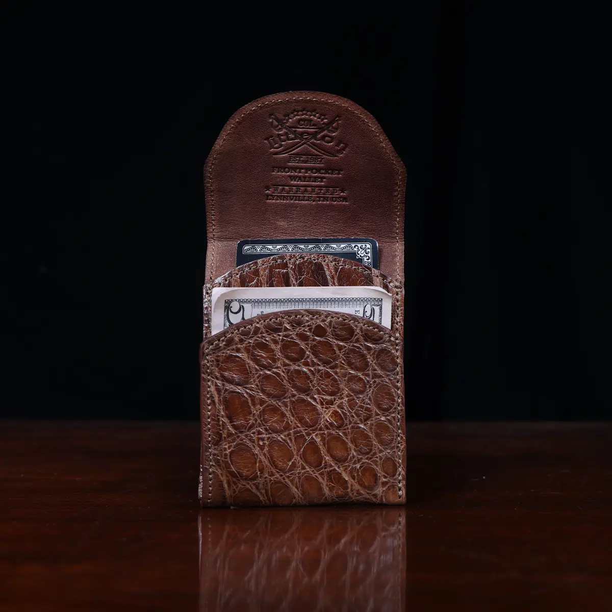 Front pocket wallet with flap in brown American Alligator - front open view with money- 002 - on wood table with a dark background