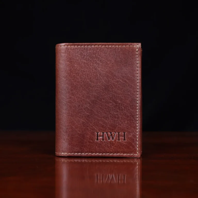 no 1 trifold wallet in brown steerhide on a wooden table with a dark background - front view