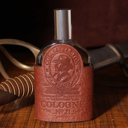 Cologne bottle sitting on wooden table with vintage sword handle behind it.