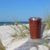 Leather tumbler sleeve for 20 ounce Yeti Rambler cup sitting on driftwood on sandy beach.