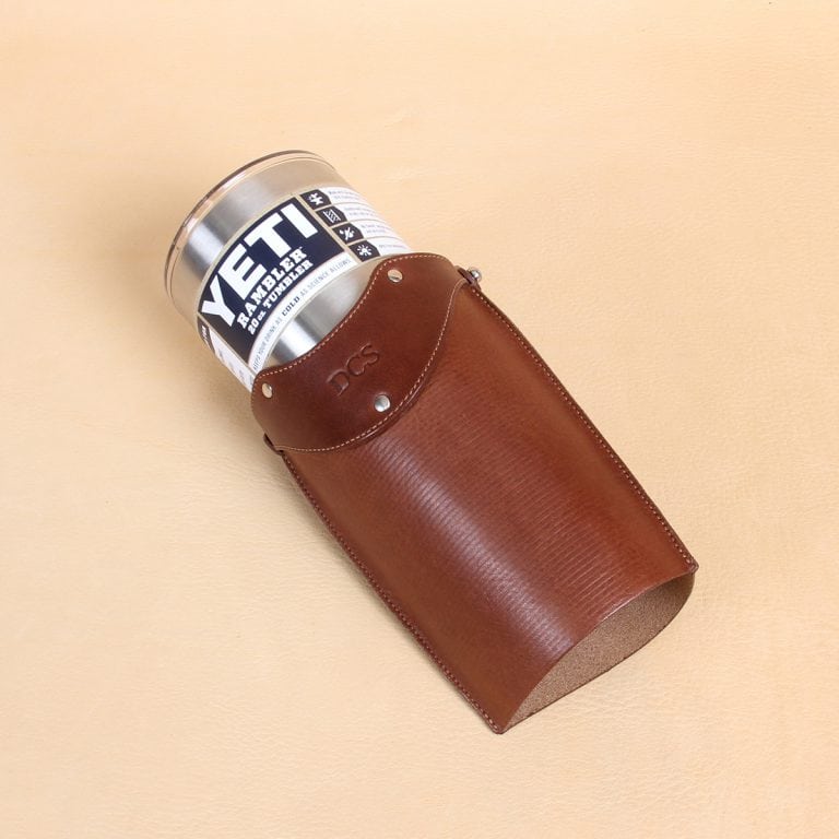 Leather tumbler sleeve for 20 ounce Yeti Rambler cup laying on side with cup coming out of sleeve.