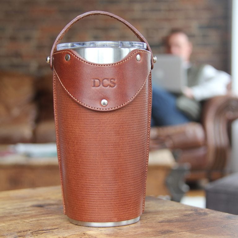 Leather tumbler sleeve for 20 ounce Yeti Rambler cup front sitting on table with carrying strap raised.
