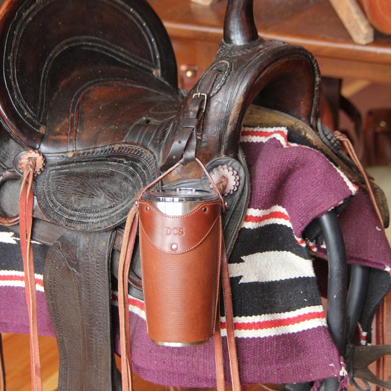 Leather tumbler sleeve for 20 ounce Yeti Rambler cup hanging by strap from handle.