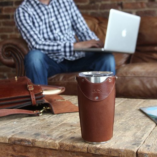 Leather tumbler sleeve for 20 ounce Yeti Rambler cup sitting on coffee table in front of man working on Mac laptop.