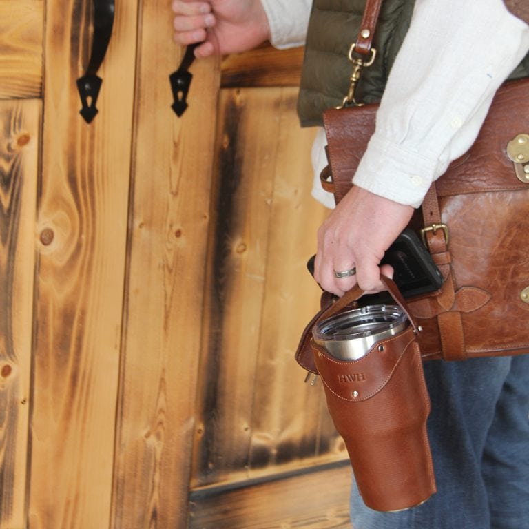 Leather tumbler sleeve for 30 ounce Yeti Rambler cup man carrying with one finger by handle headed out wooden door.