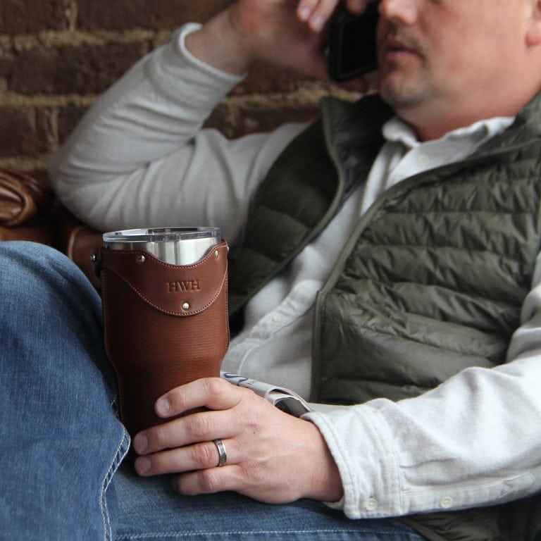 Leather tumbler sleeve for 30 ounce Yeti Rambler cup in man's hand sitting on knee.