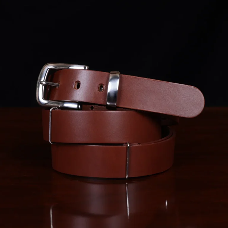no1 brown leather belt with nickel hardware - coiled front view - on a wooden table with a black background