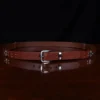 no1 brown leather belt with nickel hardware - front view - on a wooden table with a black background