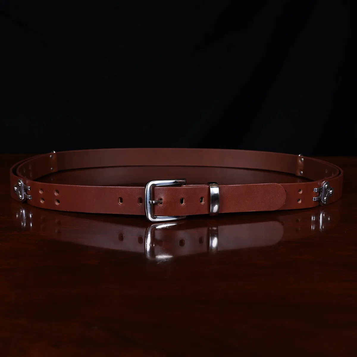 no1 brown leather belt with nickel hardware - front view - on a wooden table with a black background