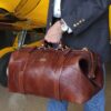 man holding large brown leather travel bag