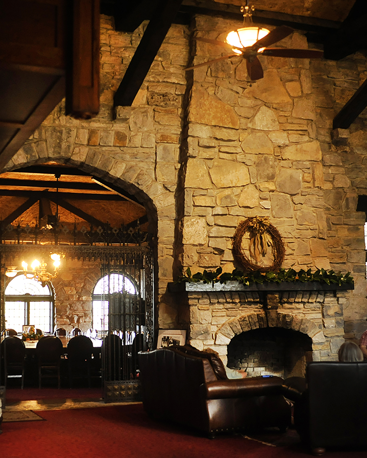 Inside the main room of the Milky Way manor house with a stone chimney and fireplace, with a view of the huge dining room and table in the background on the left.