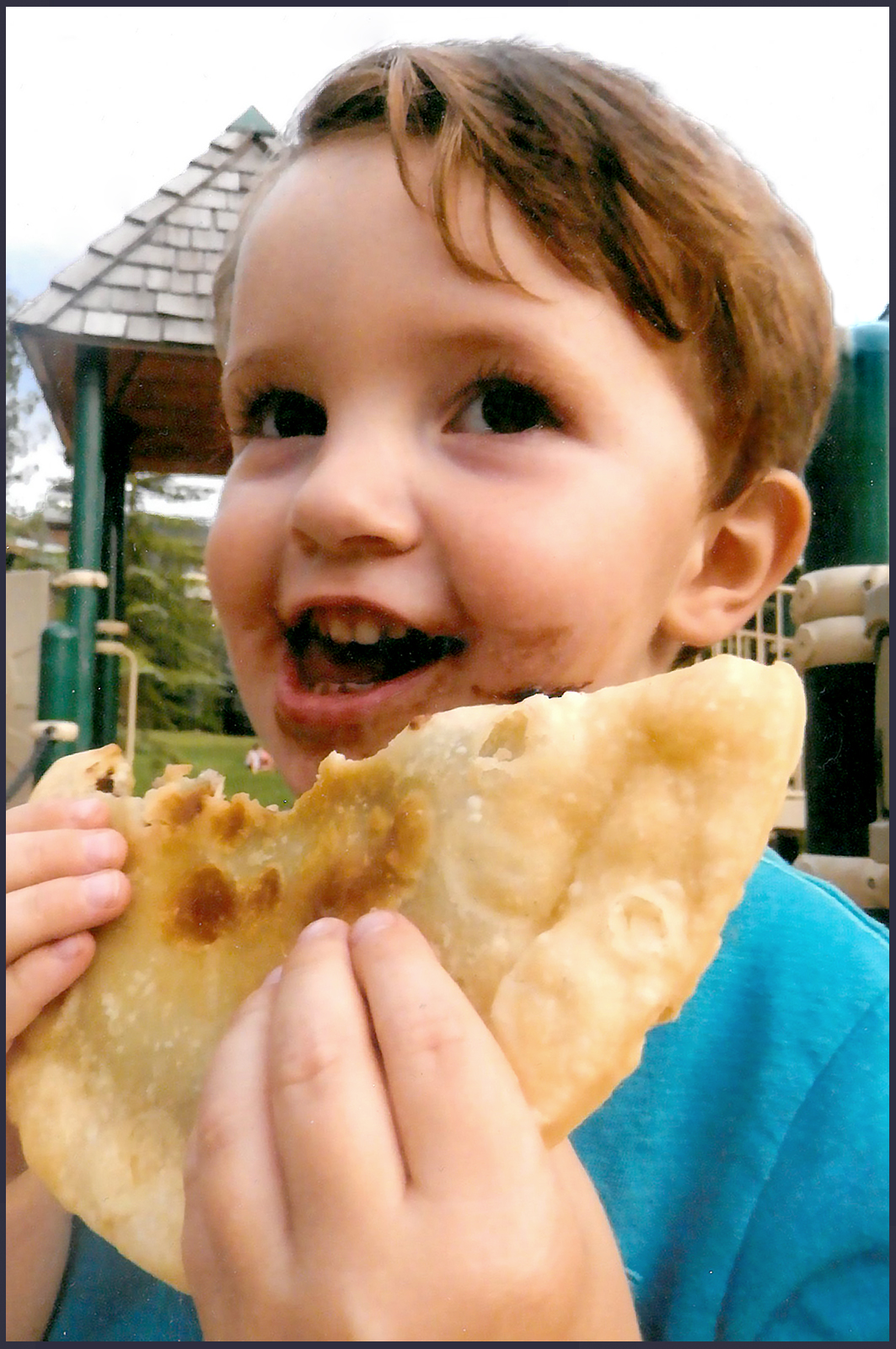 Close up of a young boy eating a fried chocolate pie.